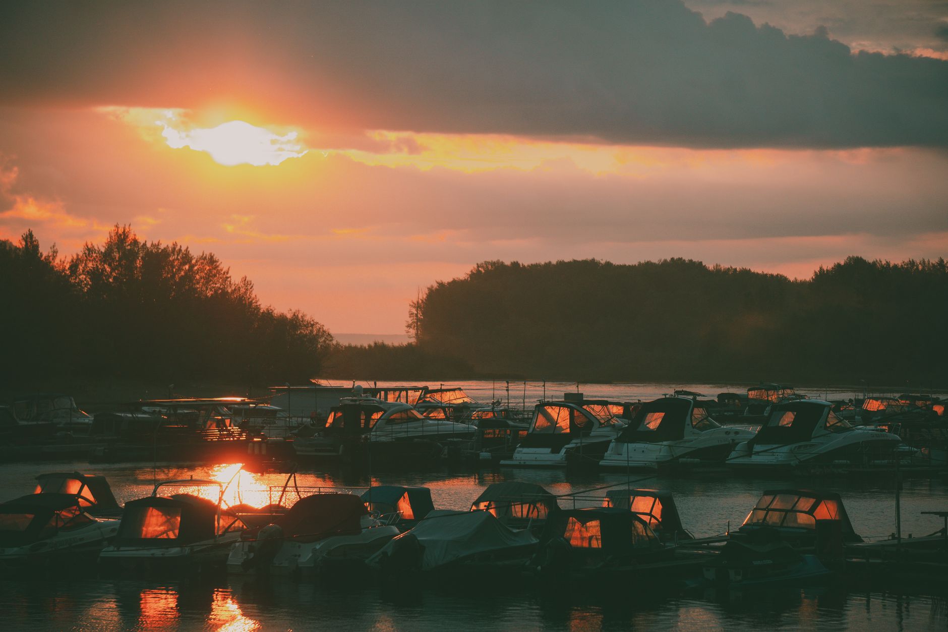 Boats docked at a lakeside marina under a fiery orange sunset