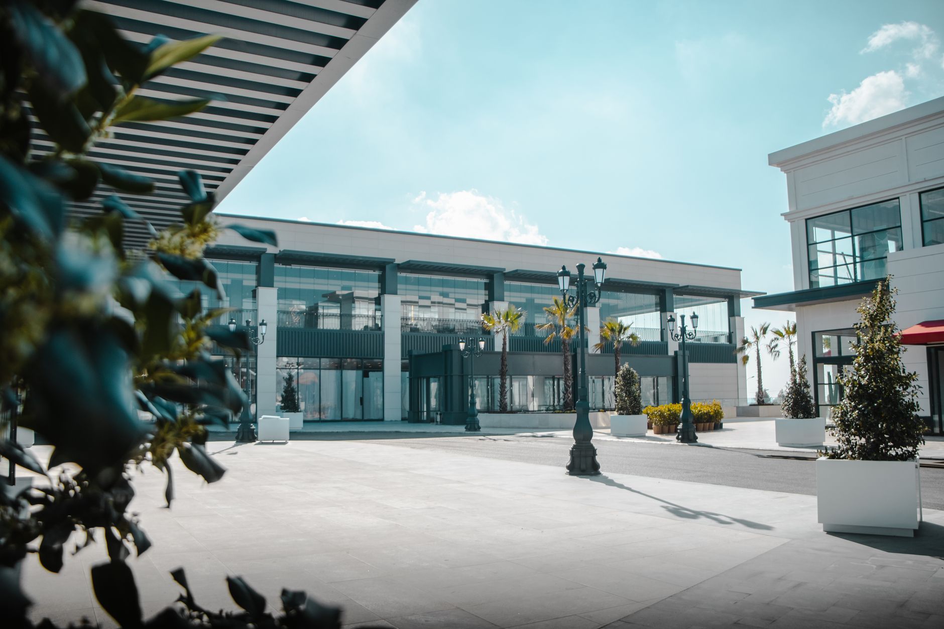 A bright modern open-air shopping plaza with lampposts and planters
