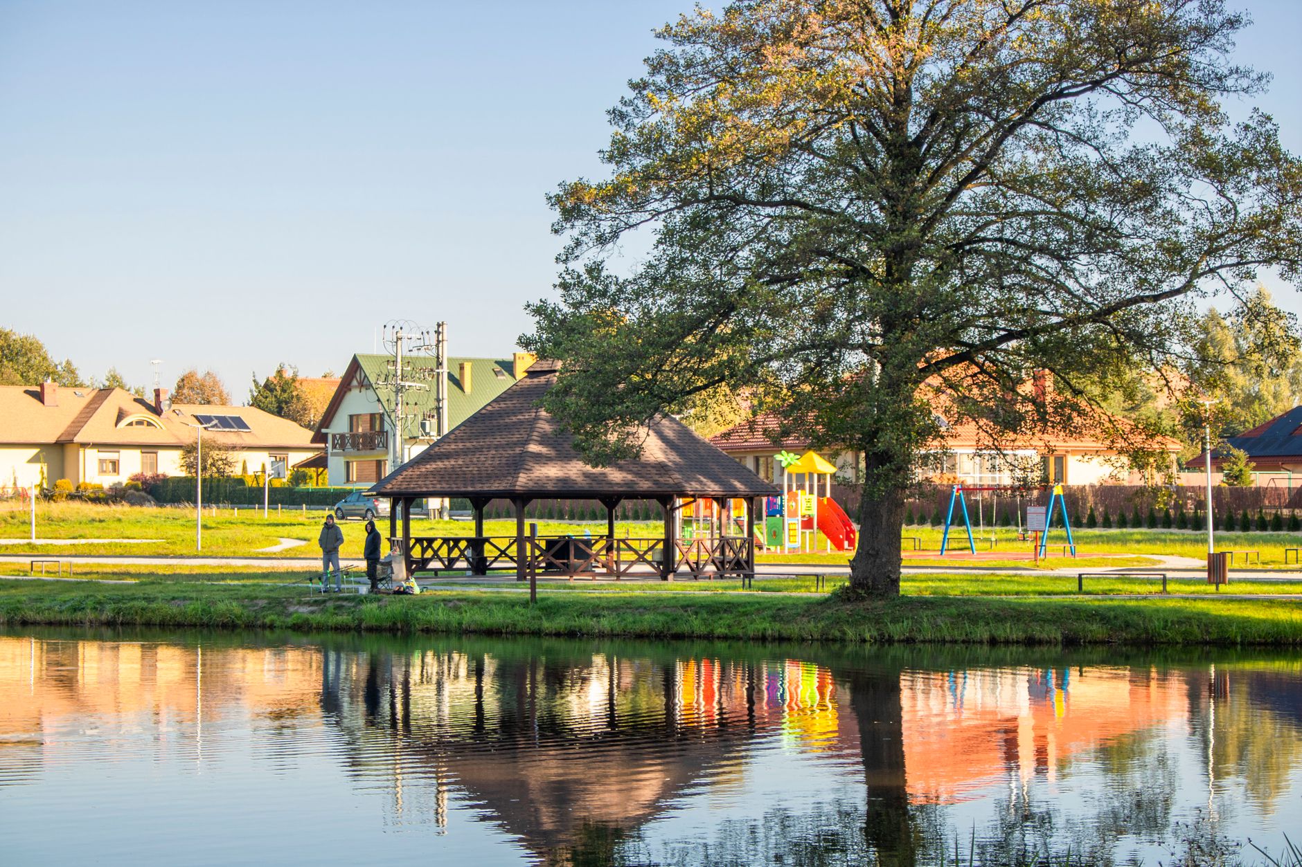 A lakeside community park with a pavilion and playground reflected in the water
